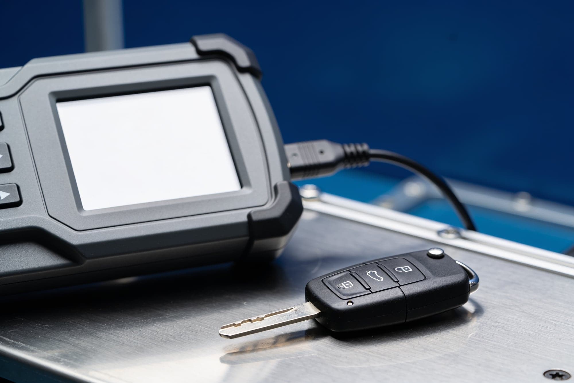 Una chiave d'auto con telecomando accanto a uno strumento di programmazione, su un banco d'acciaio