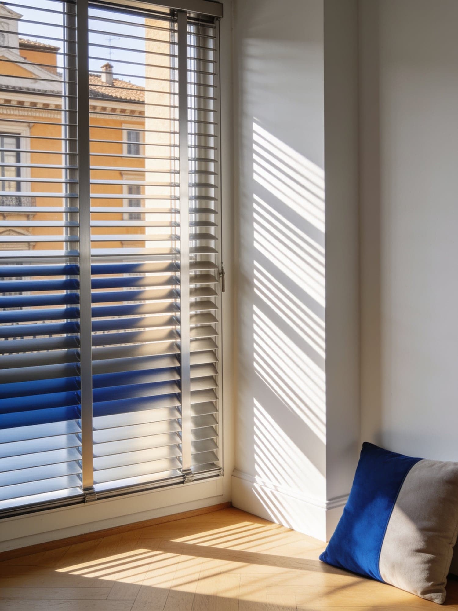 Una finestra con veneziane in alluminio socchiuse e la luce del pomeriggio a strisce sul pavimento