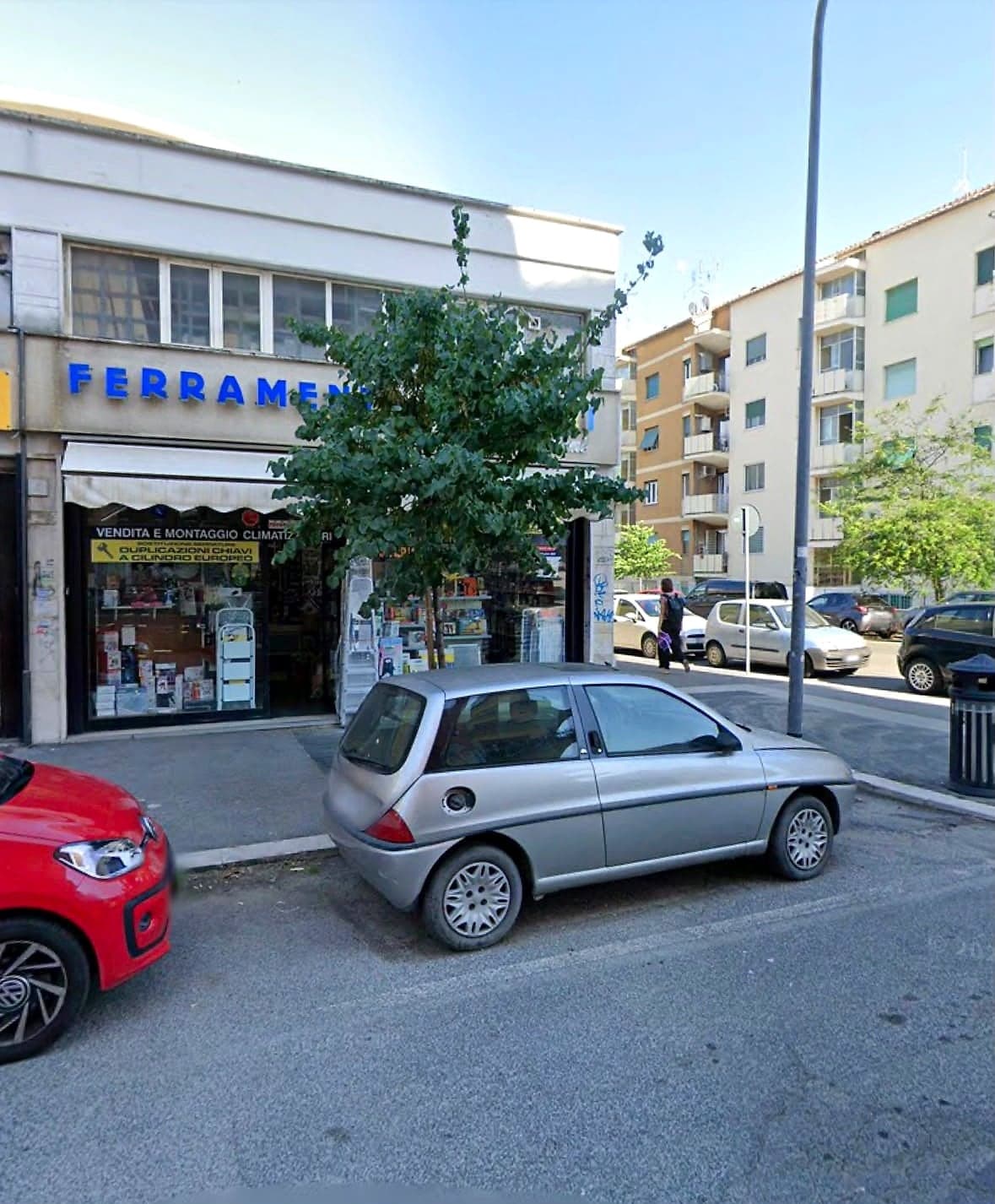 La palazzina di via Filippi con la ferramenta al piano terra, un albero e le auto parcheggiate
